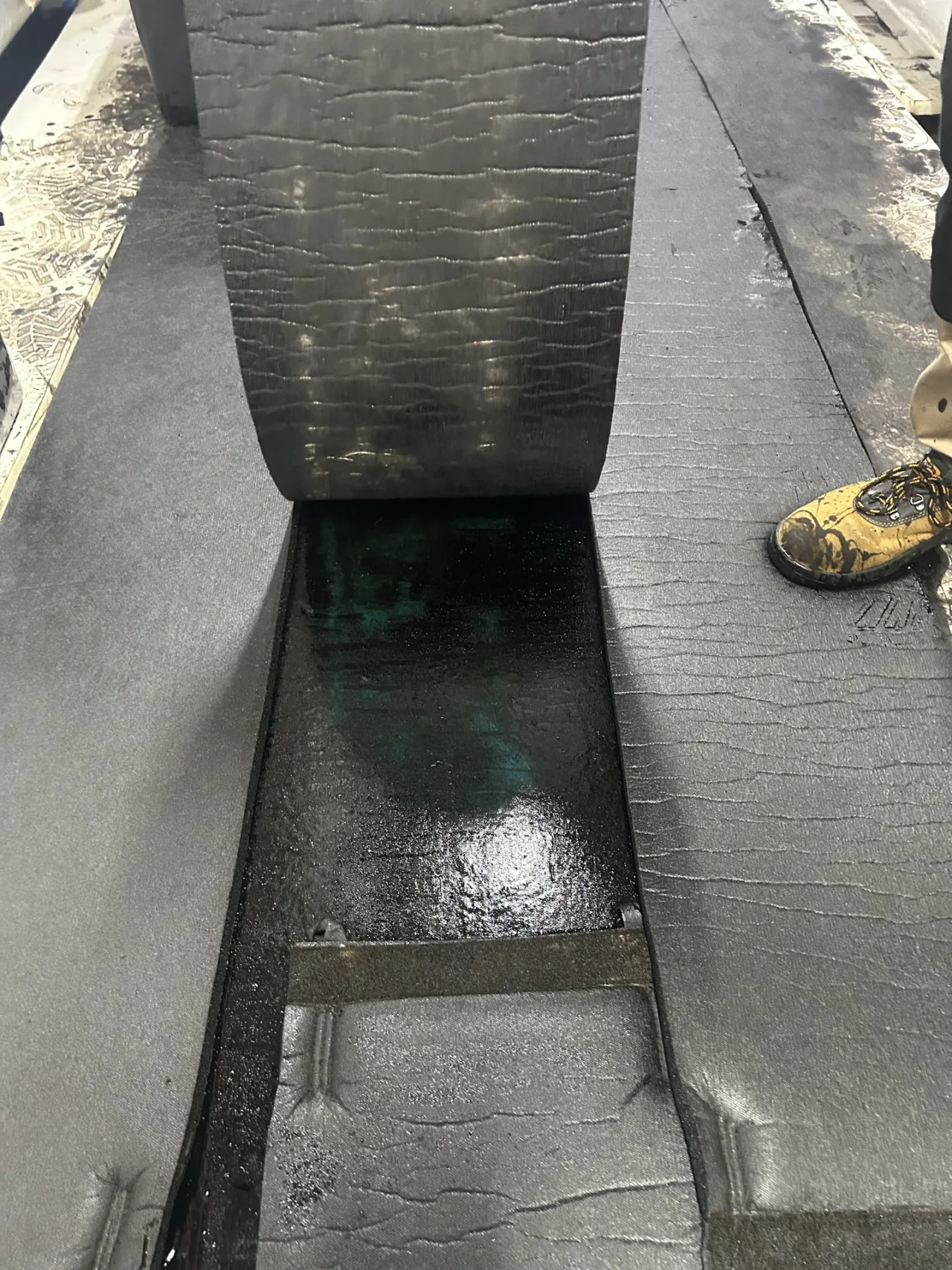 Absorbent carpet lifted to uncover the viscous fuel collected in the channel