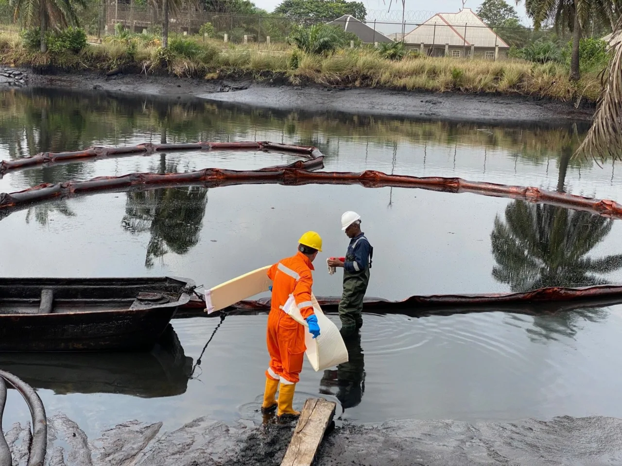 Operators handling a FoamFlex carpet at the edge of a pond enclosed by a containment boom, Ob Ob, Nigeria