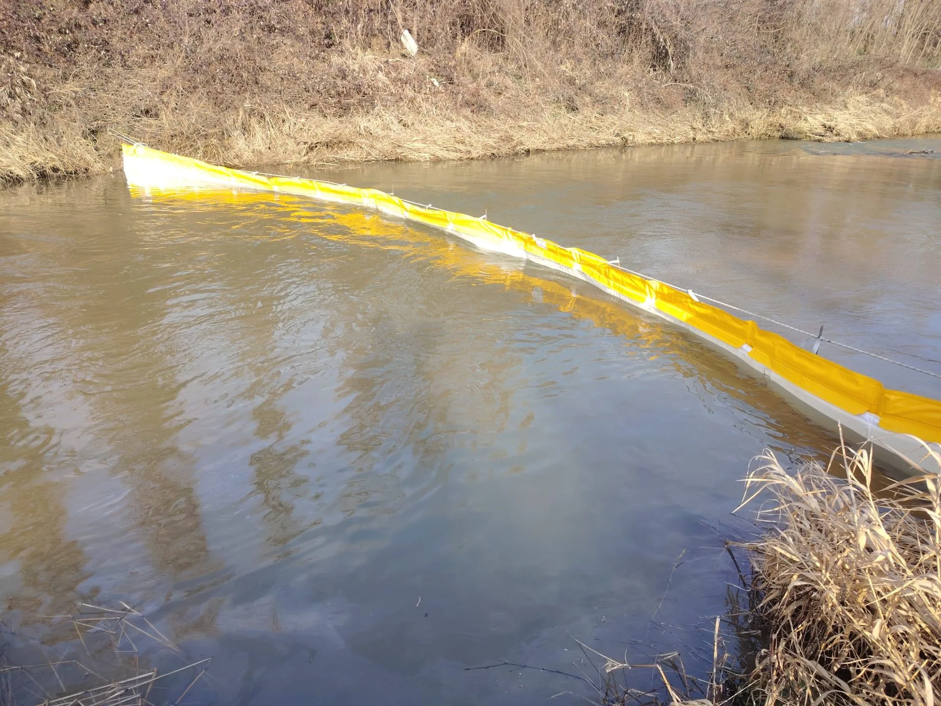 Yellow T1 barrier line floating diagonally across a watercourse to intercept surface hydrocarbons