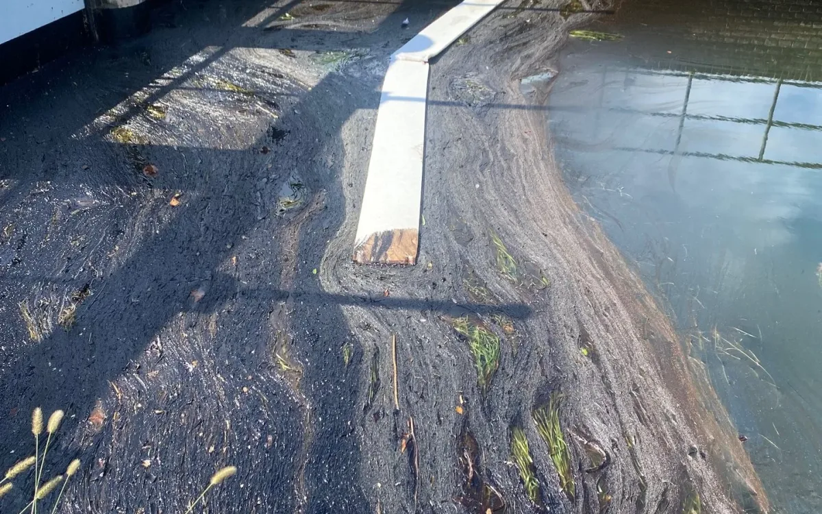 Absorbent line floating at the sluice gate over dark accumulated hydrocarbons