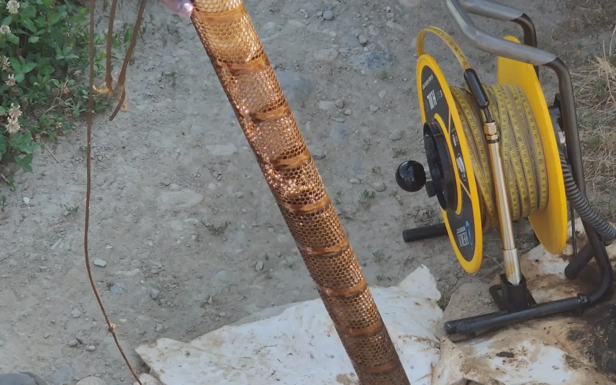Perforated cage and absorbent sock being lifted out of a piezometer, with a water level reel nearby