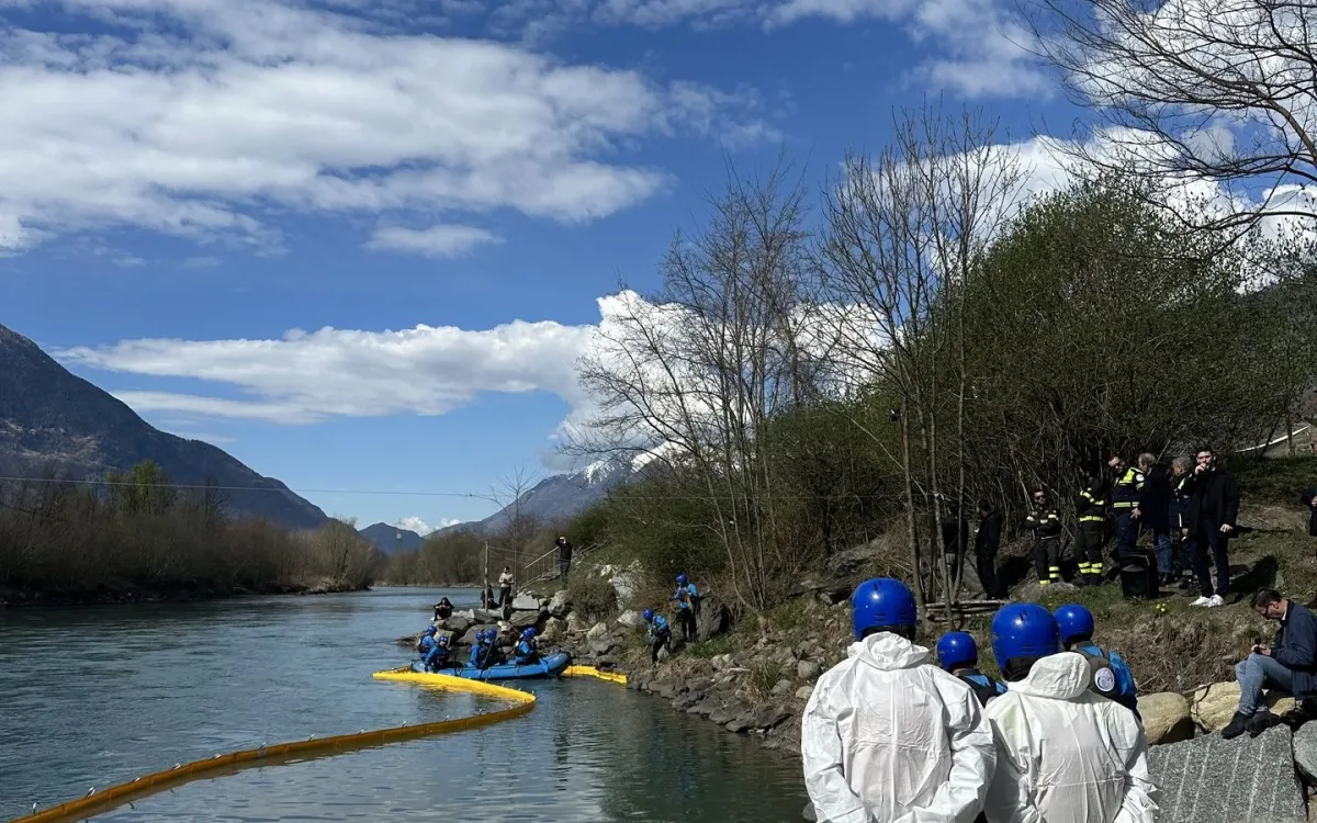 Operators in white protective suits and blue helmets on the river bank watching the boom