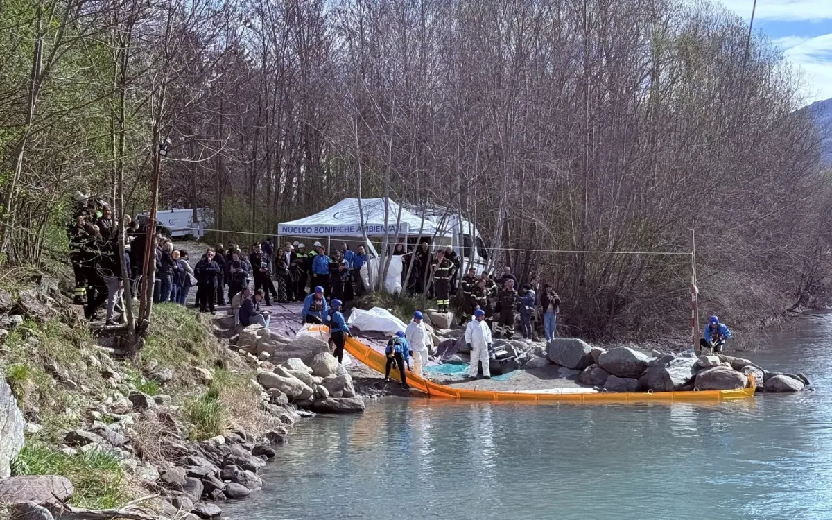 Riverbank deployment area with absorbent materials and teams working along the boom, mountains behind