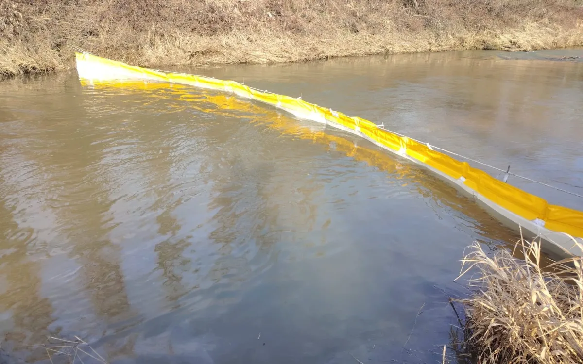 Yellow T1 barrier line floating diagonally across a watercourse to intercept surface hydrocarbons